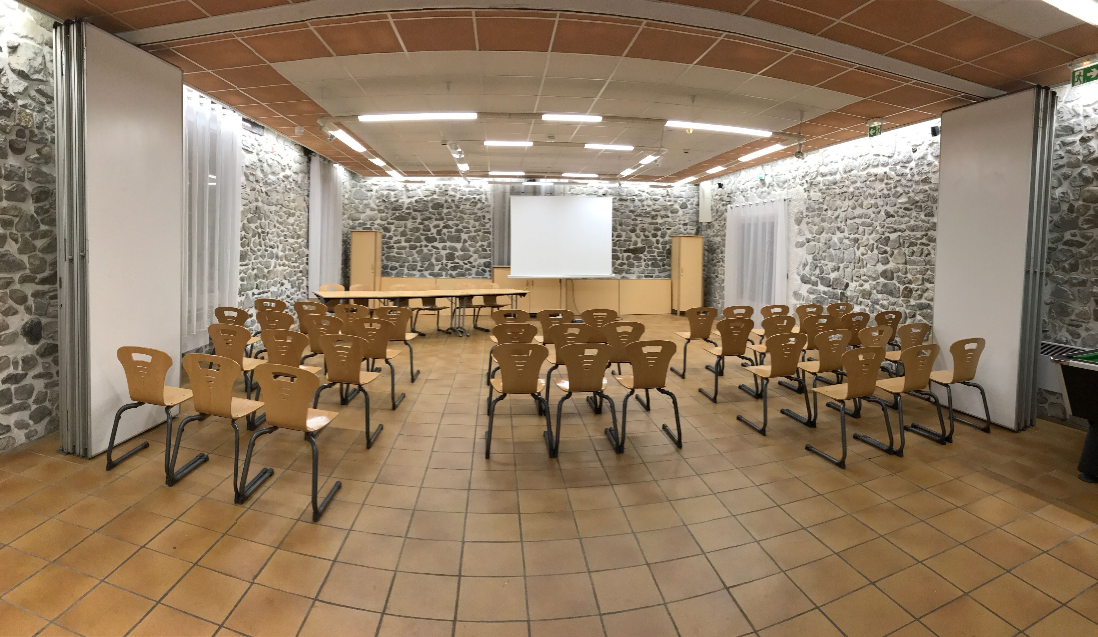 Ein Konferenzraum mit Steinwand, einer Whiteboard und mehreren in Reihen angeordneten Stühlen.