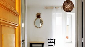 Une chambre d’hôtel avec une porte en bois, un bureau avec une chaise, un lit, un miroir rond et un luminaire suspendu.