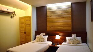 Ein Hotelzimmer mit zwei Betten, einem Holzkopfteil, Nachttischlampen und einer Wand-Klimaanlage.