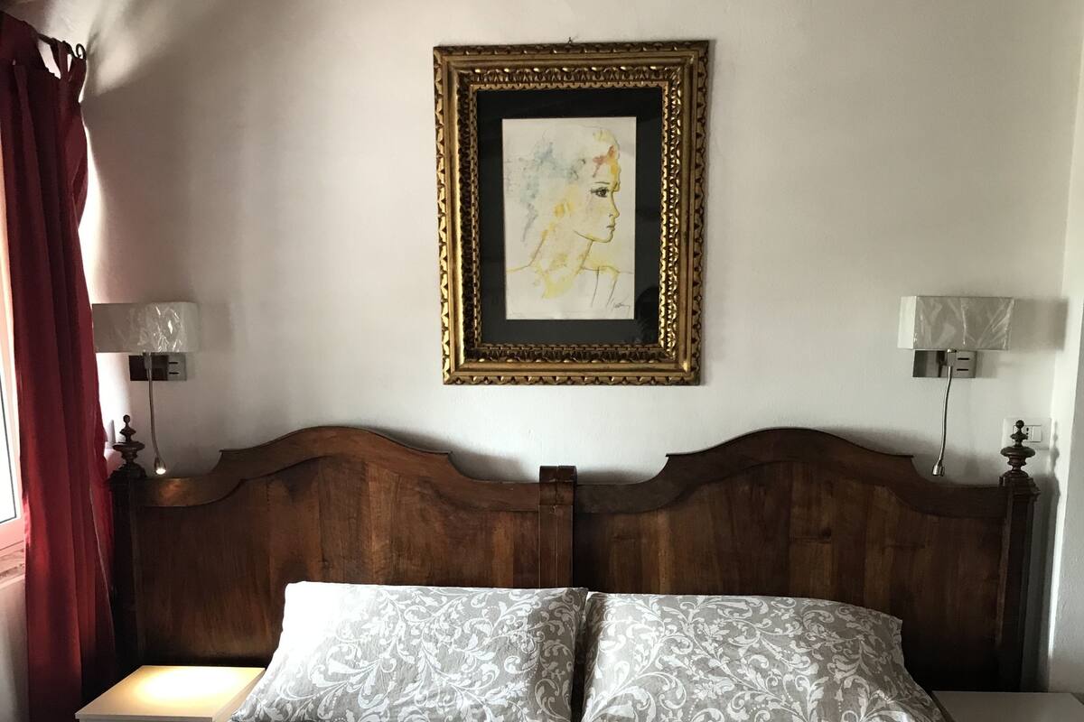 Un lit bien fait, avec une couvre-lit à motifs, une tête de lit en bois et une œuvre d’art encadrée au-dessus.