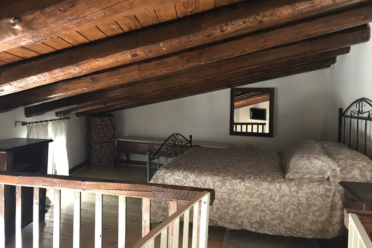 Une pièce rustique avec un plafond en bois, un lit recouvert d’une literie à motifs, une petite table et une chaise.