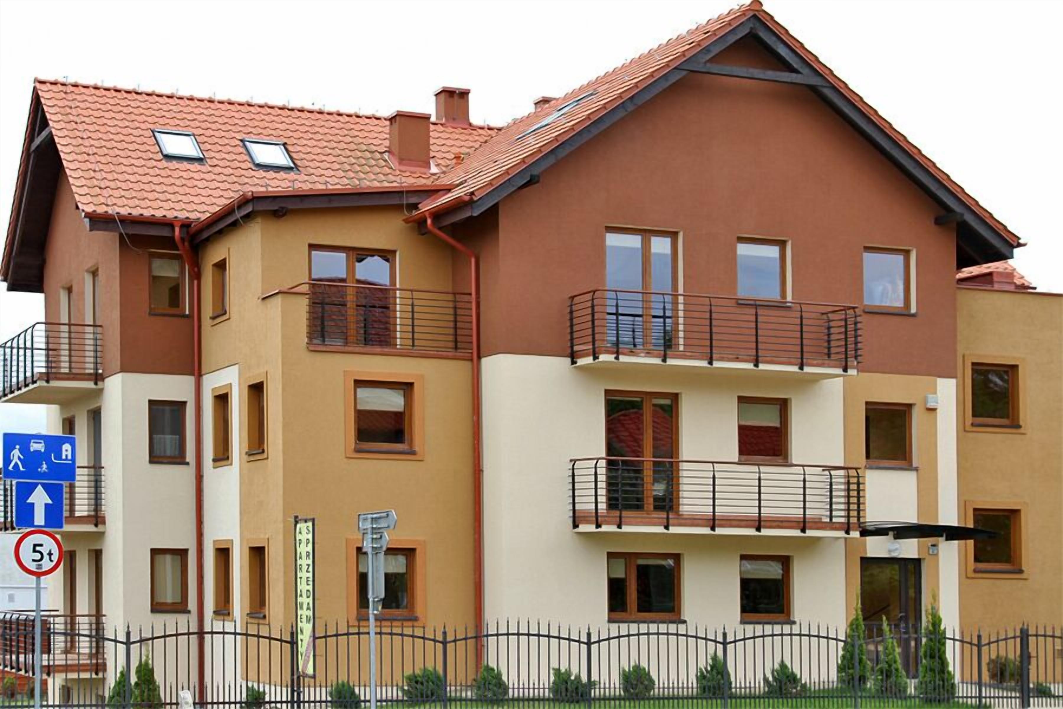 A multi-story residential building with a red-tiled roof, balconies, and a pedestrian access sign.