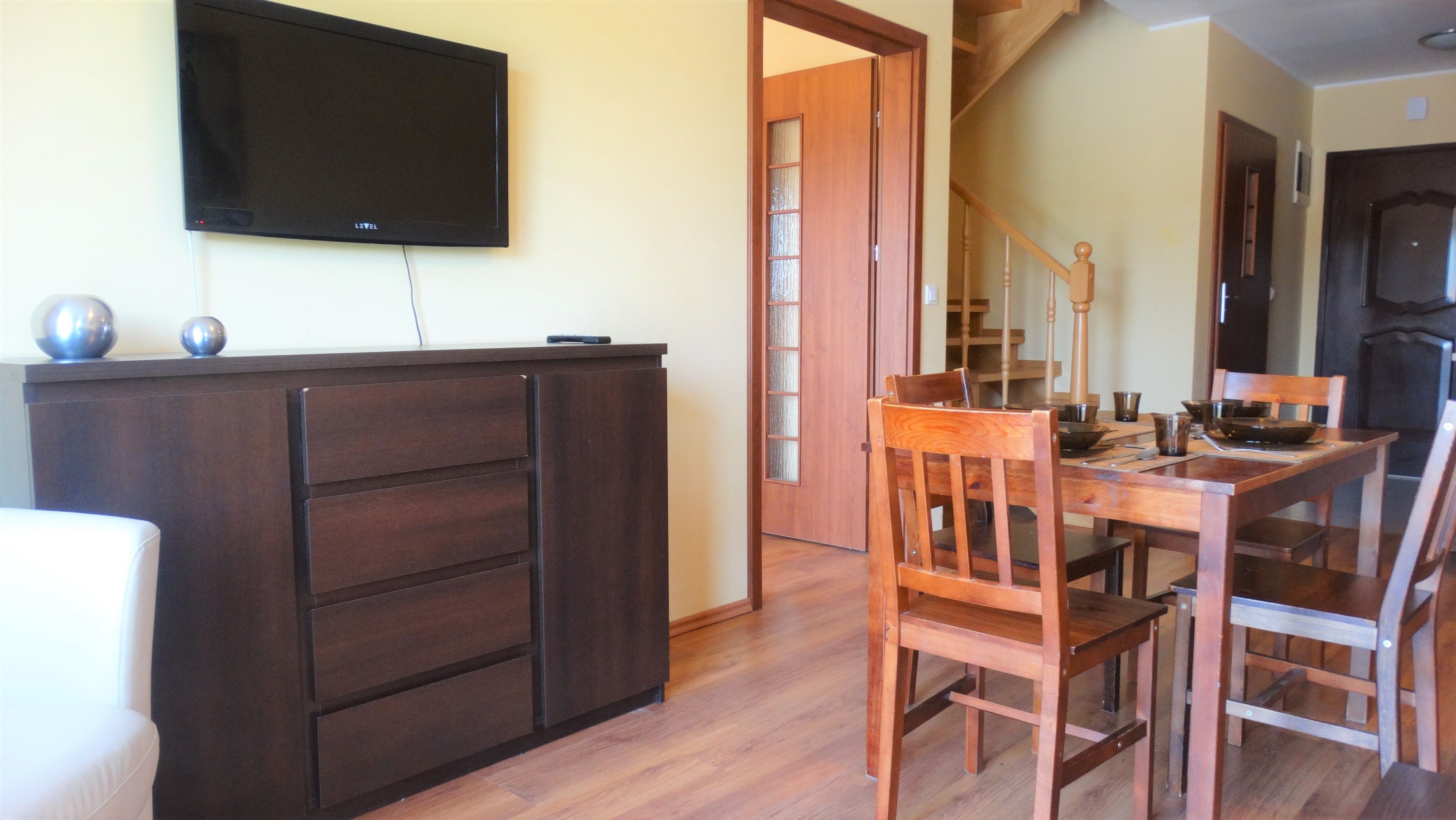Ein Essbereich mit einem Holztisch und -stühlen, einem dunklen Holzschrank und einem an der Wand montierten Flachbildfernseher.