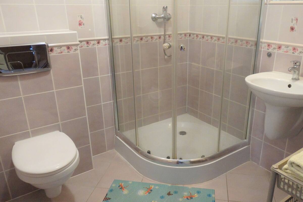 A bathroom with a glass-enclosed shower, a toilet, a sink, and a basket of towels.