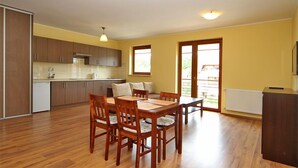 A spacious kitchen with wooden cabinets, a dining table with chairs, and a large window providing natural light. - HoliApart Gdanska 52 (Krynica Morska)