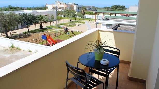 A balcony with a table and chairs, a potted plant, and a view of a playground with a slide. - B&B La Sciuscitta (Morciano di Leuca)