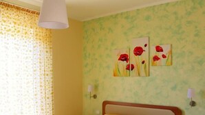 A bedroom with a wooden bed, two bedside tables, a nightstand, and a wall with three paintings. - B&B La Sciuscitta (Morciano di Leuca)