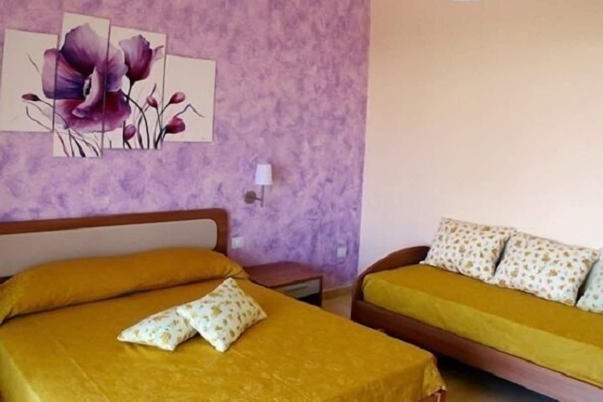 Une chambre avec deux lits, chacun agrémenté de draps jaunes et d’oreillers à motifs, un mur violet et un luminaire au plafond.