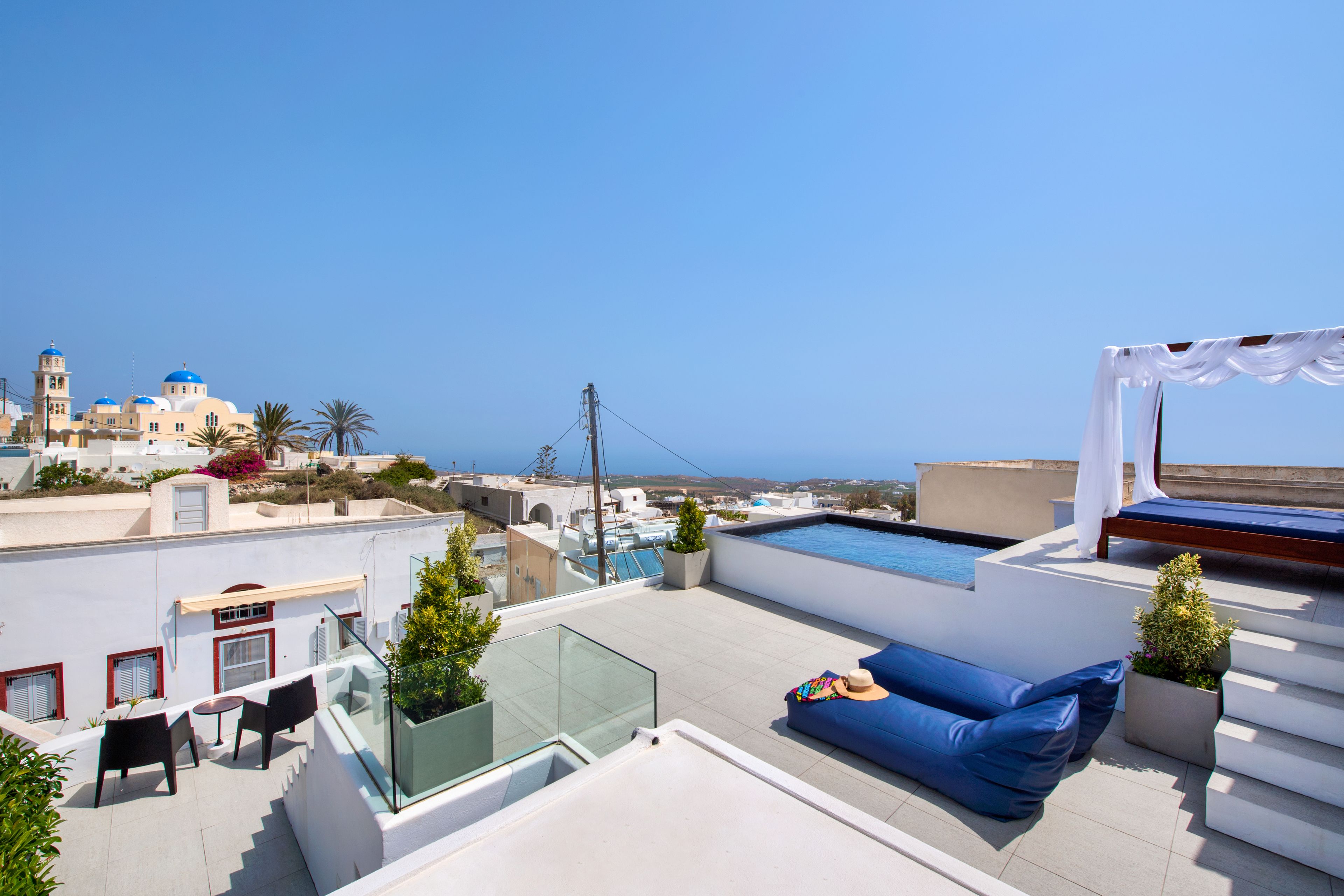 Um terraço no terraço com piscina, assentos azuis e vista para o mar e edifícios.