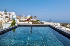 A swimming pool with clear blue water, surrounded by white buildings with blue domes, and a view of the sea in the background. - Mirinda Villa (Santorini)