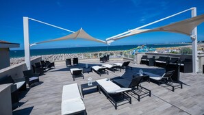 A rooftop terrace with lounge chairs and umbrellas, overlooking a beach and a water park. - Hotel Baby (Rimini)