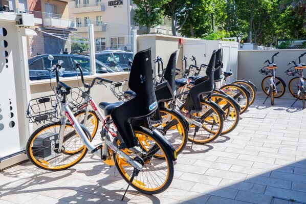 A row of bicycles with attached seats and baskets, parked on a tiled surface.