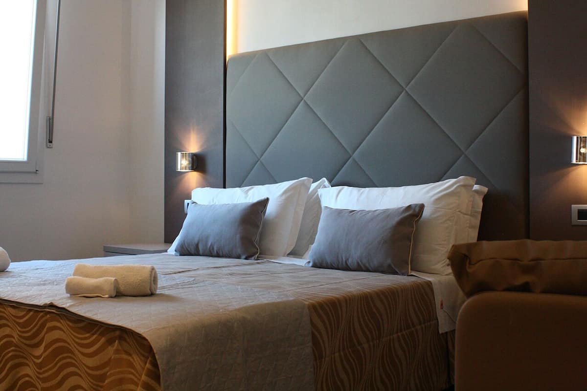 A hotel room with a large bed, grey headboard, and two bedside lamps.