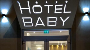 A hotel entrance with a neon sign reading "HOTEL BABY" and a reception desk visible inside. - Hotel Baby (Rimini)