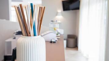 Un vase blanc avec des baguettes en bois, un bureau, une lampe et un téléviseur dans une pièce au style moderne.