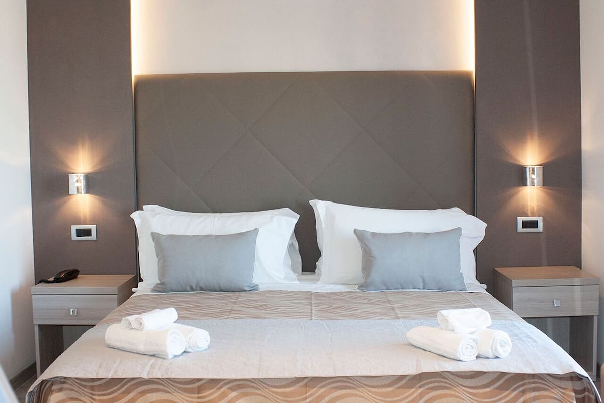 A hotel room with a large bed, two bedside tables, and wall-mounted lights.