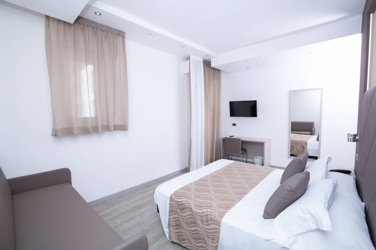 A modern hotel room with a bed, a desk, a chair, a television, and a large window with curtains.