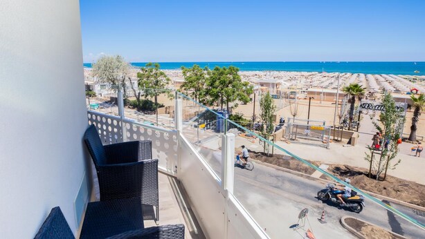 A balcony with a view of a beach and a road with vehicles. - Hotel Baby (Rimini)