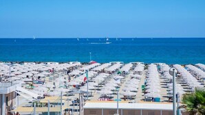 A beachside hotel with rows of sunbeds and umbrellas, a clear view of the sea, and sailboats in the distance. - Hotel Baby (Rimini)