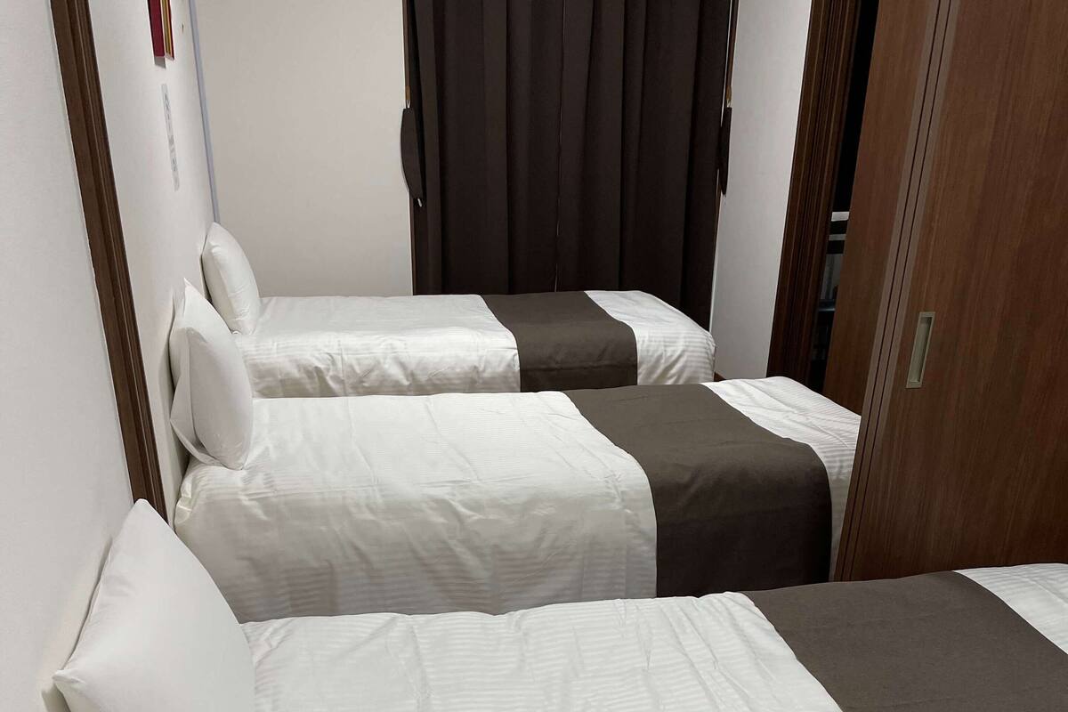 Une chambre d’hôtel avec deux lits, chacun agrémenté de draps blancs et d’un élément décoratif de couleur foncée.