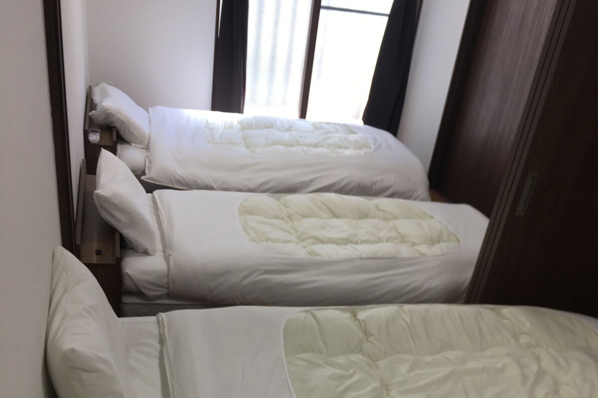 Habitación de hotel con tres camas, cada una con ropa blanca y un edredón acolchado.