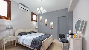 A bedroom with a bed, bedside table, lamp, dresser, mirror, and wall sconces. - Centro Houses (Santorini)