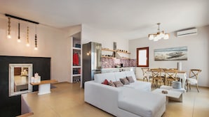 A modern living room with a white sofa, a dining area with wooden furniture, and a kitchen in the background. - Centro Houses (Santorini)