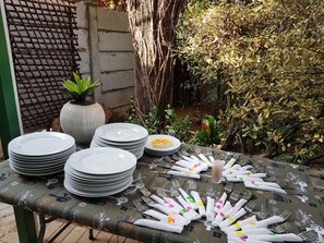 A table set with plates, cutlery, and napkins, surrounded by greenery and a brick wall. - Gemstone Guest House (Klerksdorp)