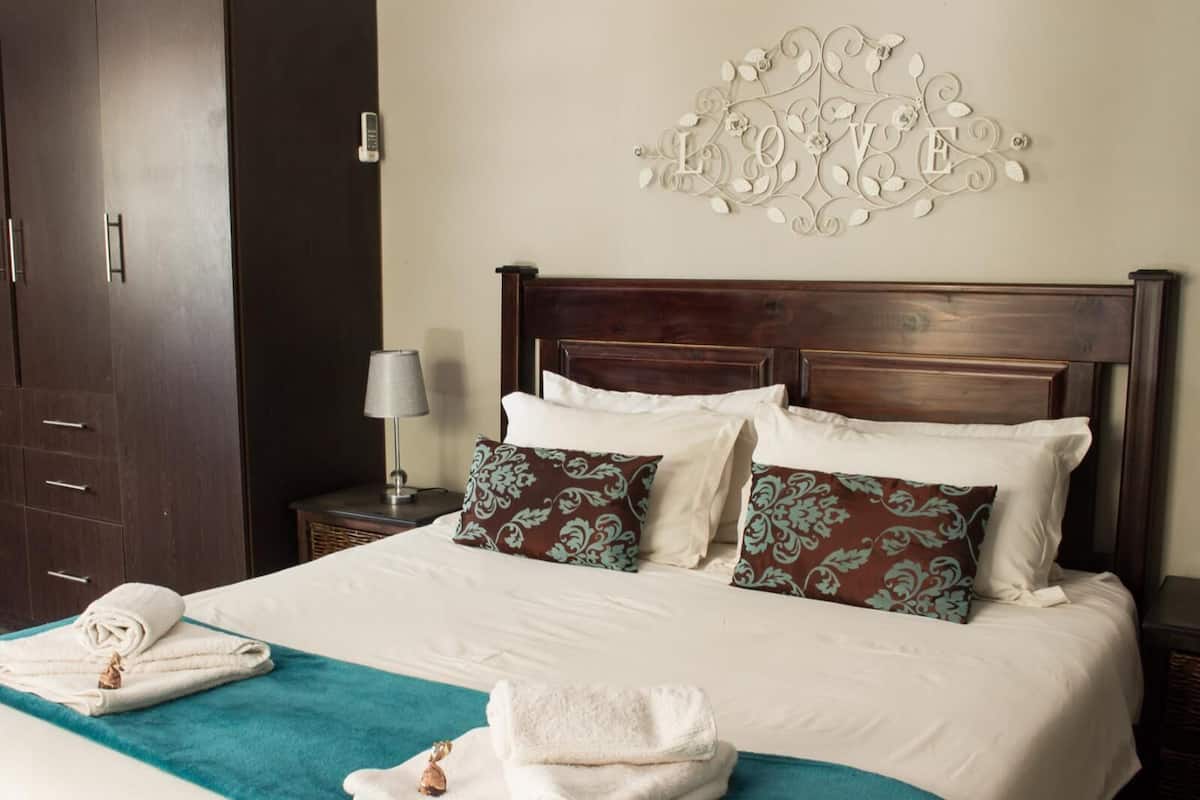 A neatly made bed with white linens and teal accents, a wooden headboard, and a decorative wall piece above.