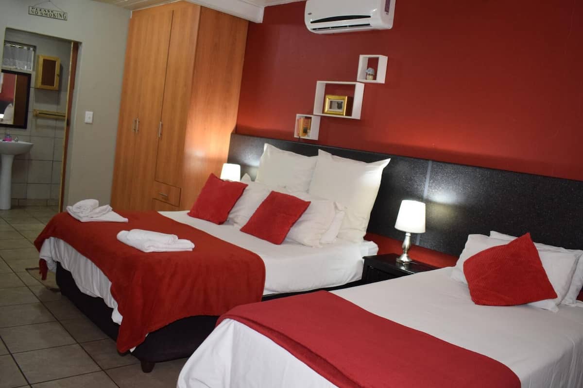 A hotel room with two beds, red and white bedding, a wooden wardrobe, a sink, and an air conditioning unit.