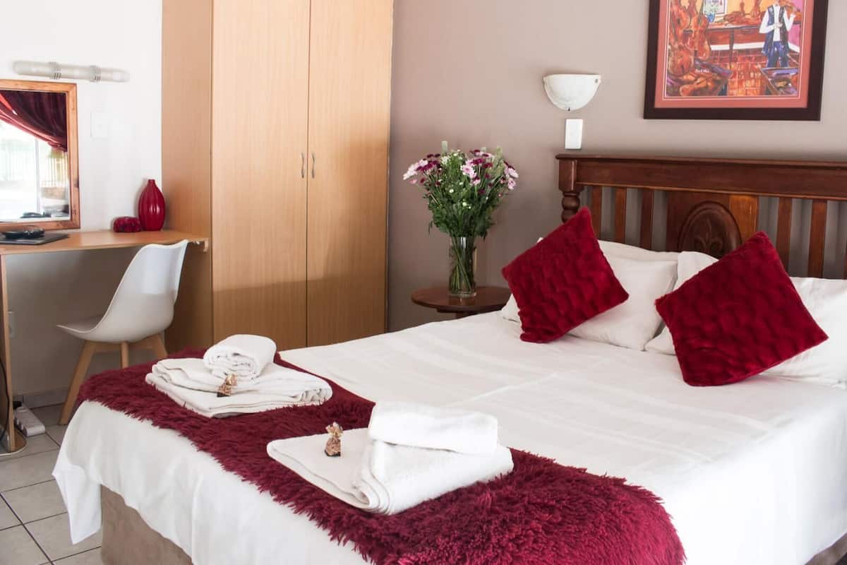 A hotel room with a bed, a desk, a chair, a nightstand, and a painting on the wall.