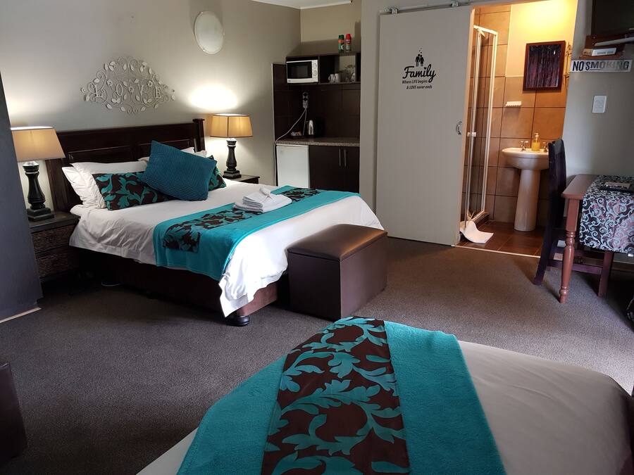 Habitación de hotel con cama, lámparas de noche, escritorio, silla, microondas, lavamanos y cartel de 'No Fumar'.