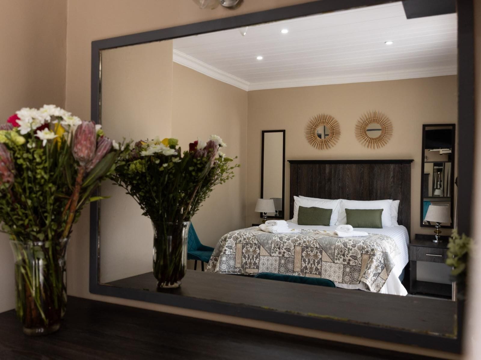 A bedroom with a large bed, two bedside tables, a mirror, and a decorative wall piece.