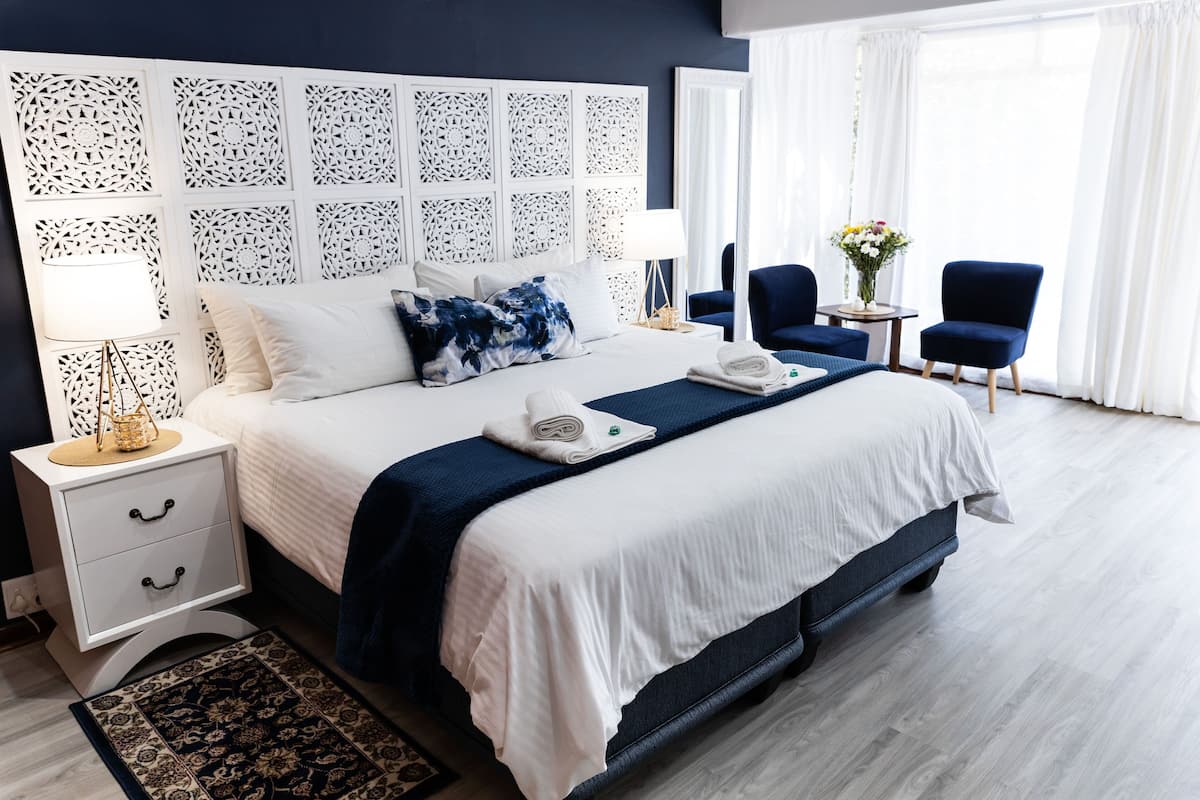 A neatly arranged hotel room with a large bed, a bedside table with a lamp, two chairs, and a small table with a vase of flowers.
