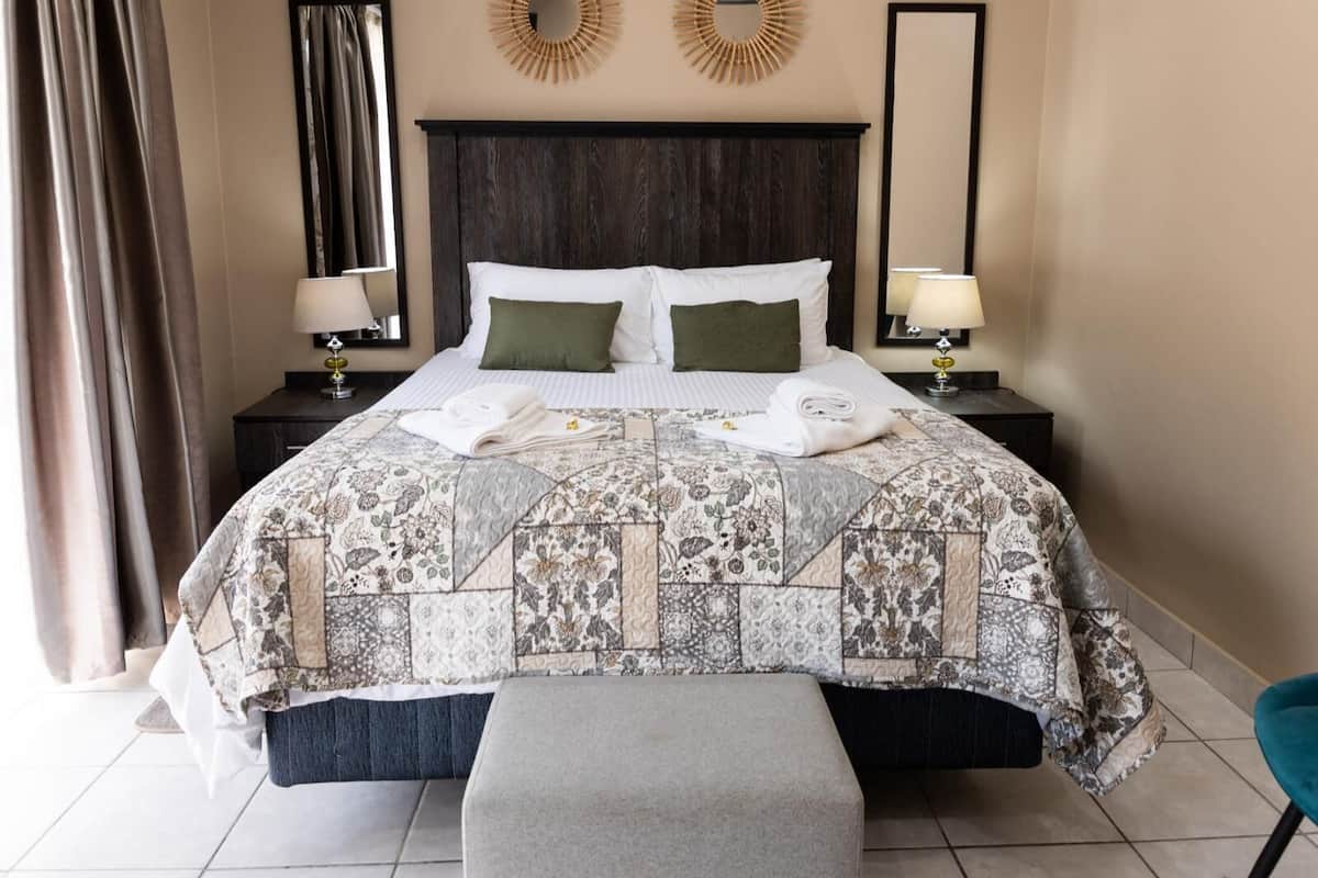 A hotel room with a large bed, two bedside tables with lamps, a headboard, and two wall mirrors.
