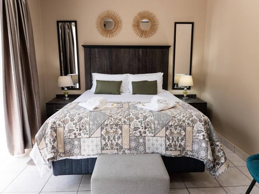A hotel room with a large bed, two bedside tables with lamps, a headboard, and two wall mirrors.
