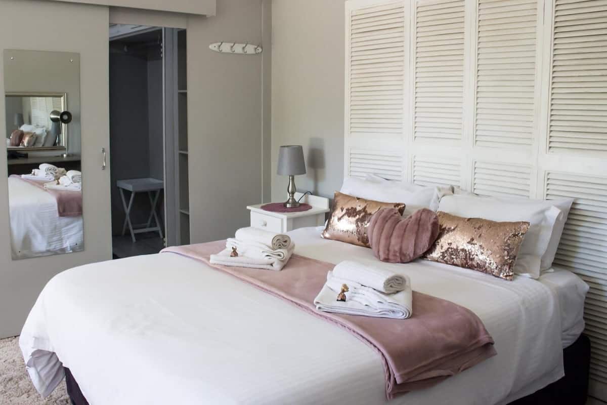 A neatly arranged bedroom with a large bed, a bedside table with a lamp, and a mirror.