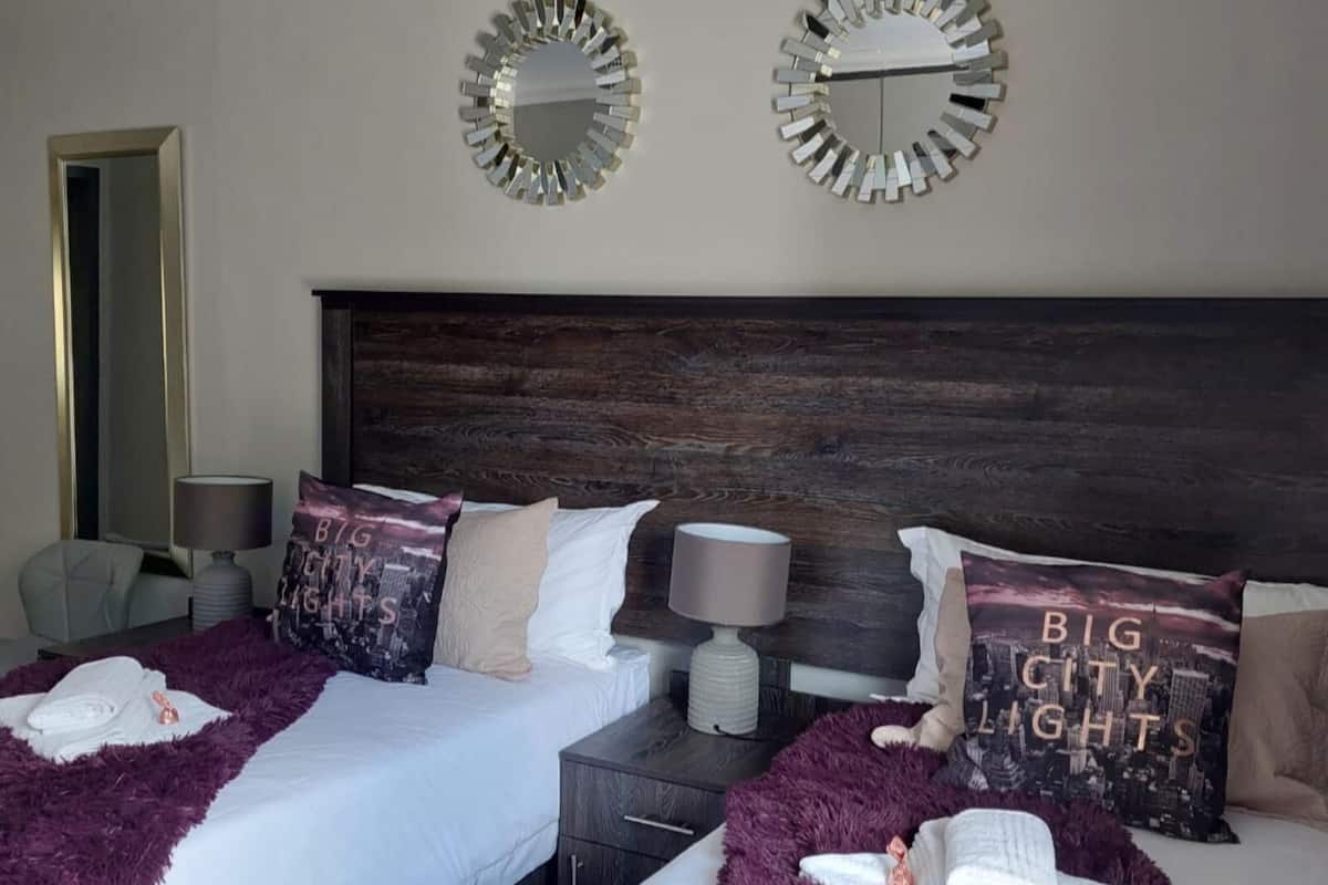 A hotel room with a large bed, two nightstands, a wooden headboard, and two wall mirrors.
