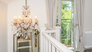 Uma escadaria com um candelabro, uma janela com cortinas e vista para o verde lá fora.