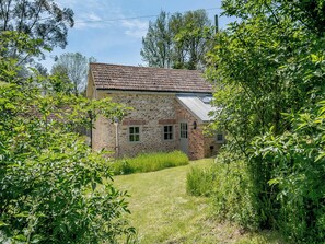 A stone house with a tiled roof, surrounded by lush greenery and trees.