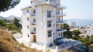 Un edificio de varios pisos con balcones, un estacionamiento y vistas al mar y a las montañas.