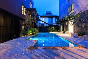A modern swimming pool with a tiled deck, surrounded by buildings with large windows and a covered walkway. - Prima House Pattaya (Pattaya)