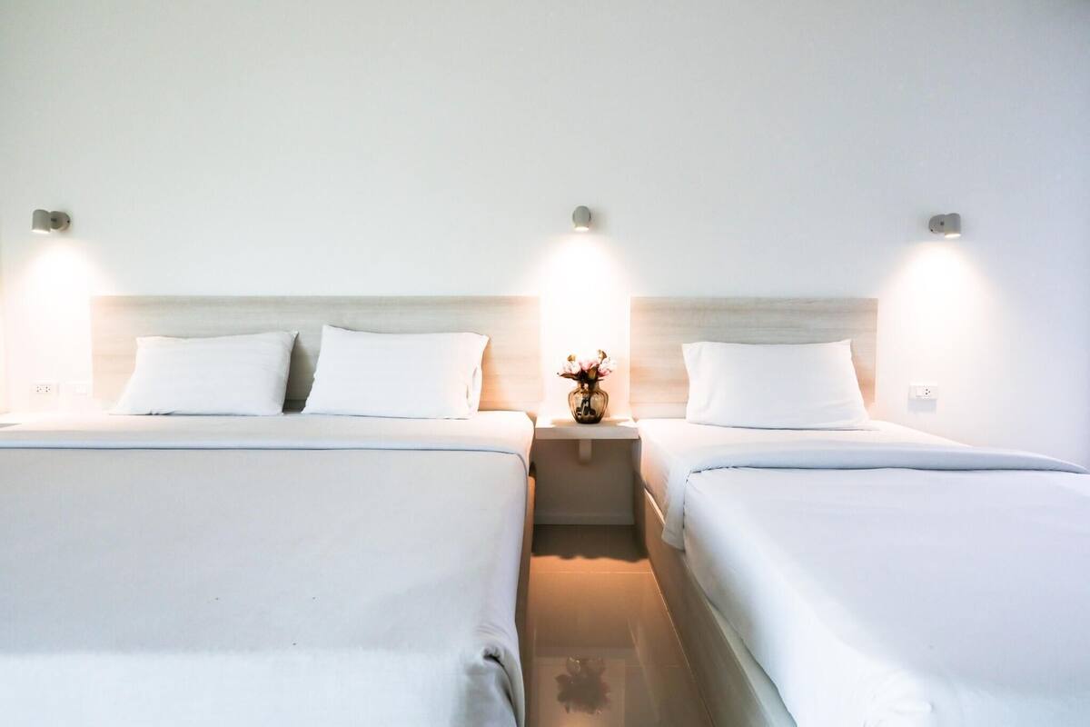 A hotel room with two beds, each with white linens, a nightstand with a vase of flowers, and wall-mounted lighting.