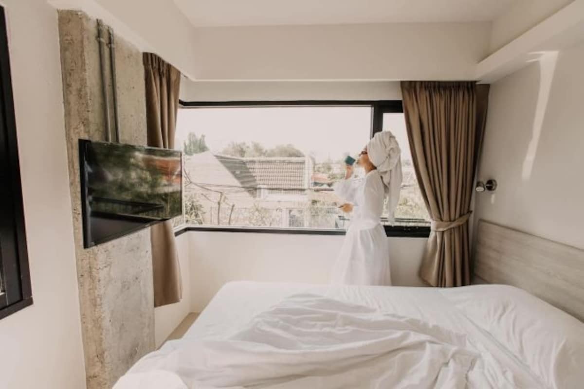 A hotel room with a bed, a TV mounted on the wall, and a view of the outside.