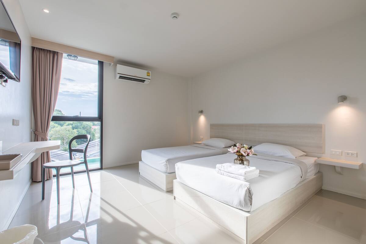 A modern hotel room with two beds, a desk, and a chair.