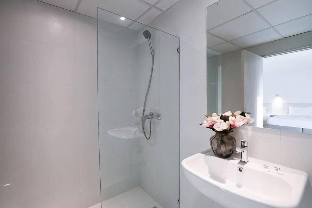 A modern bathroom with a glass shower enclosure, a white sink, and a vase with flowers.