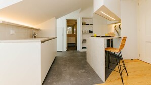 A modern kitchen with a built-in island, a bar stool, and a view into the dining area. - Boho Studio (Lisboa ciudad)