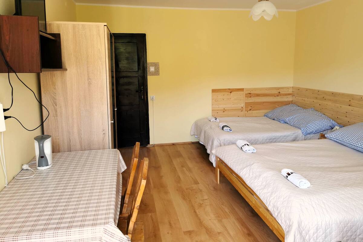 Ein Hotelzimmer mit zwei Betten, Holz-Kopfteilen, einem Schreibtisch mit kariertem Tischläufer, einem Wasserkocher und einem Wand-Fernseher.