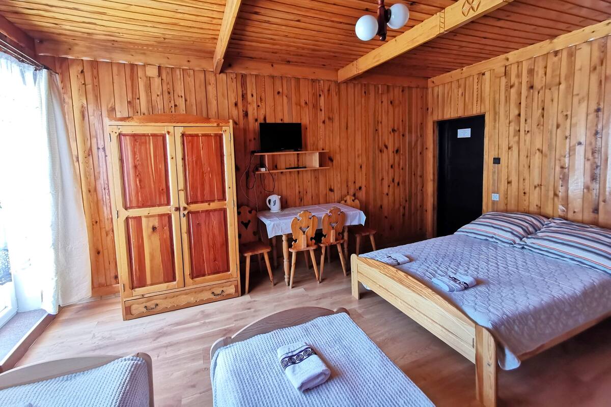 Ein Zimmer einer Holzhütte mit einem Bett, einem Tisch mit Stühlen, einem Fernseher und einem Kleiderschrank.