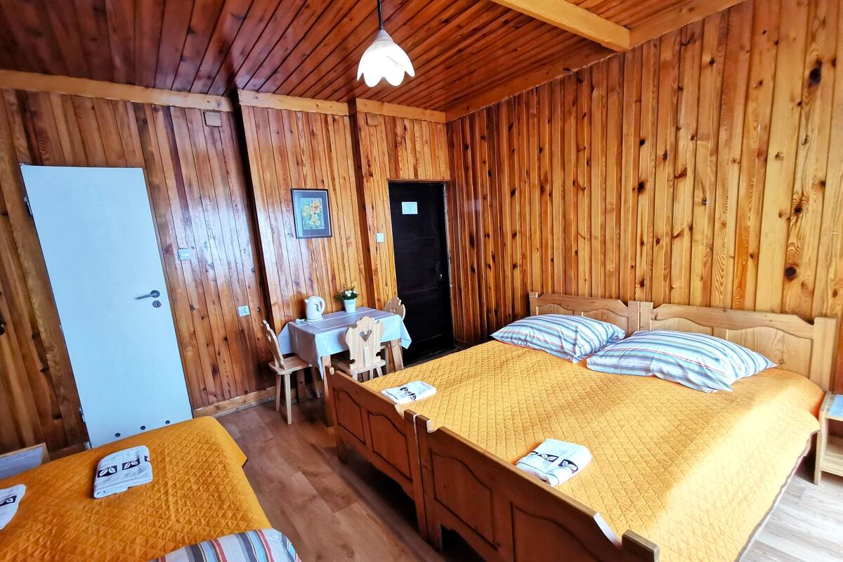 Ein Zimmer mit Holzboden, einem Bett, einem kleinen Tisch mit Stühlen und einer Tür.